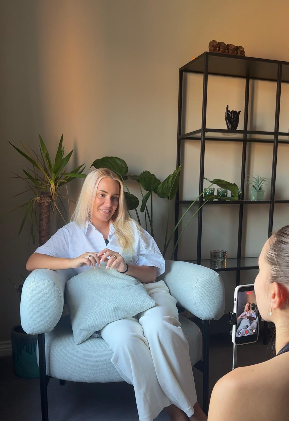 Rugile being filmed for Mind Bridge content in a blue armchair